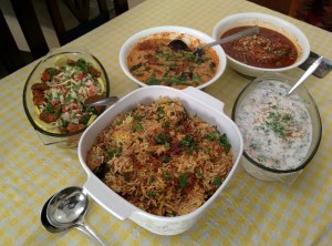 An array of goodies: chicken biryani, onion raita, mutton korma, baingan mirch ka salan, salad.